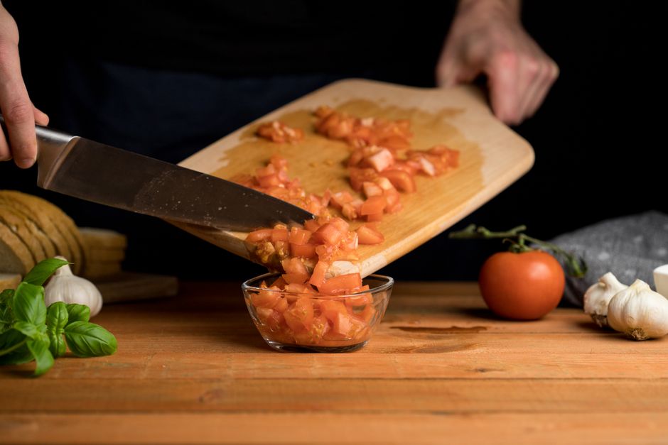 Longevidade — Chopped tomatoes being prepared on a wooden cutting board with fresh ingredients nearby.